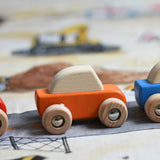A close up of the orange coloured Bajo pull back action wooden toy car placed on the road printed onto the building site Wonderie wonder cloth. These heirloom quality toys by Bajo are part of a wide range of wooden toys available here at Babipur. 