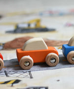 A close up of the orange coloured Bajo pull back action wooden toy car placed on the road printed onto the building site Wonderie wonder cloth. These heirloom quality toys by Bajo are part of a wide range of wooden toys available here at Babipur. 