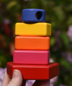 Bajo pyramid sorting board and stacker toy assembled on the base pole piece and shown in an adult's hand.