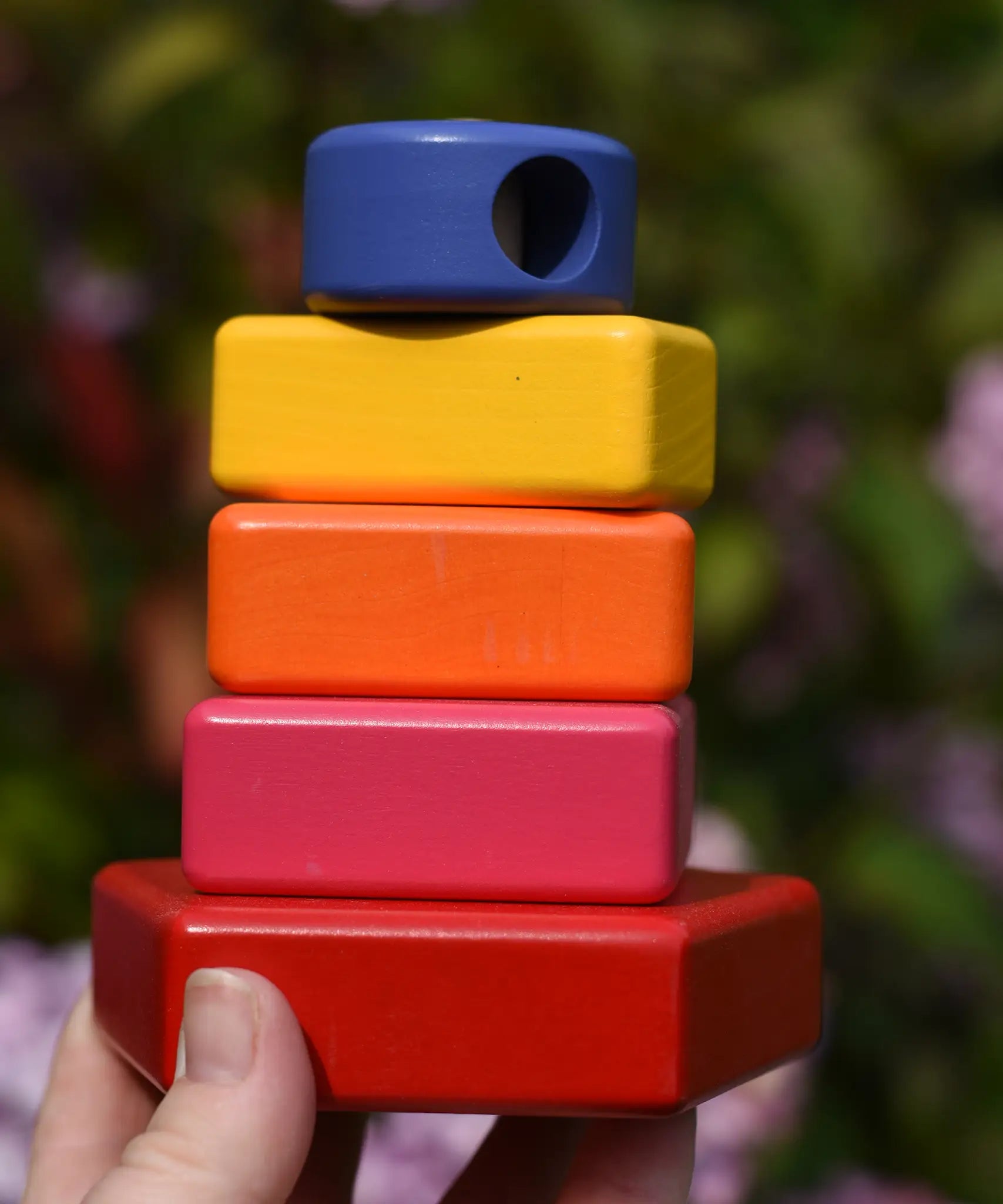 Bajo pyramid sorting board and stacker toy assembled on the base pole piece and shown in an adult's hand.
