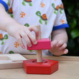 Child playing with the Bajo pyramid sorting board and stacker toy placing a pink square piece on the base piece. 