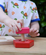 Child playing with the Bajo pyramid sorting board and stacker toy placing a pink square piece on the base piece. 