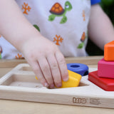 Child playing with the Bajo pyramid sorting board and stacker toy placing a yellow rectangle piece in the wooden base board frame. 