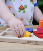 Child playing with the Bajo pyramid sorting board and stacker toy placing a yellow rectangle piece in the wooden base board frame. 