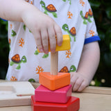 Child playing with the Bajo pyramid sorting board and stacker toy placing a yellow rectangle piece on the stacking pole. 