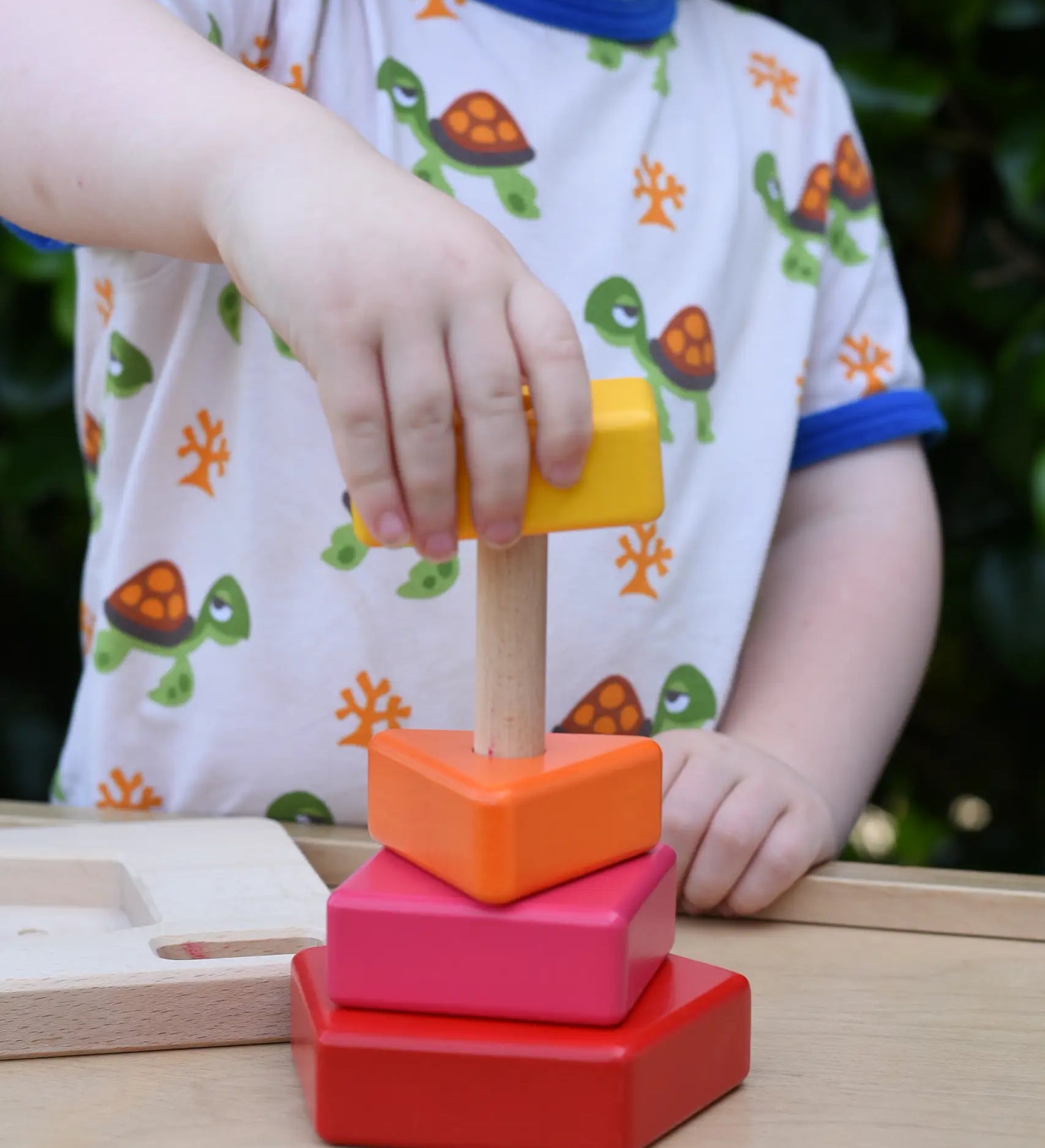 Child playing with the Bajo pyramid sorting board and stacker toy placing a yellow rectangle piece on the stacking pole. 