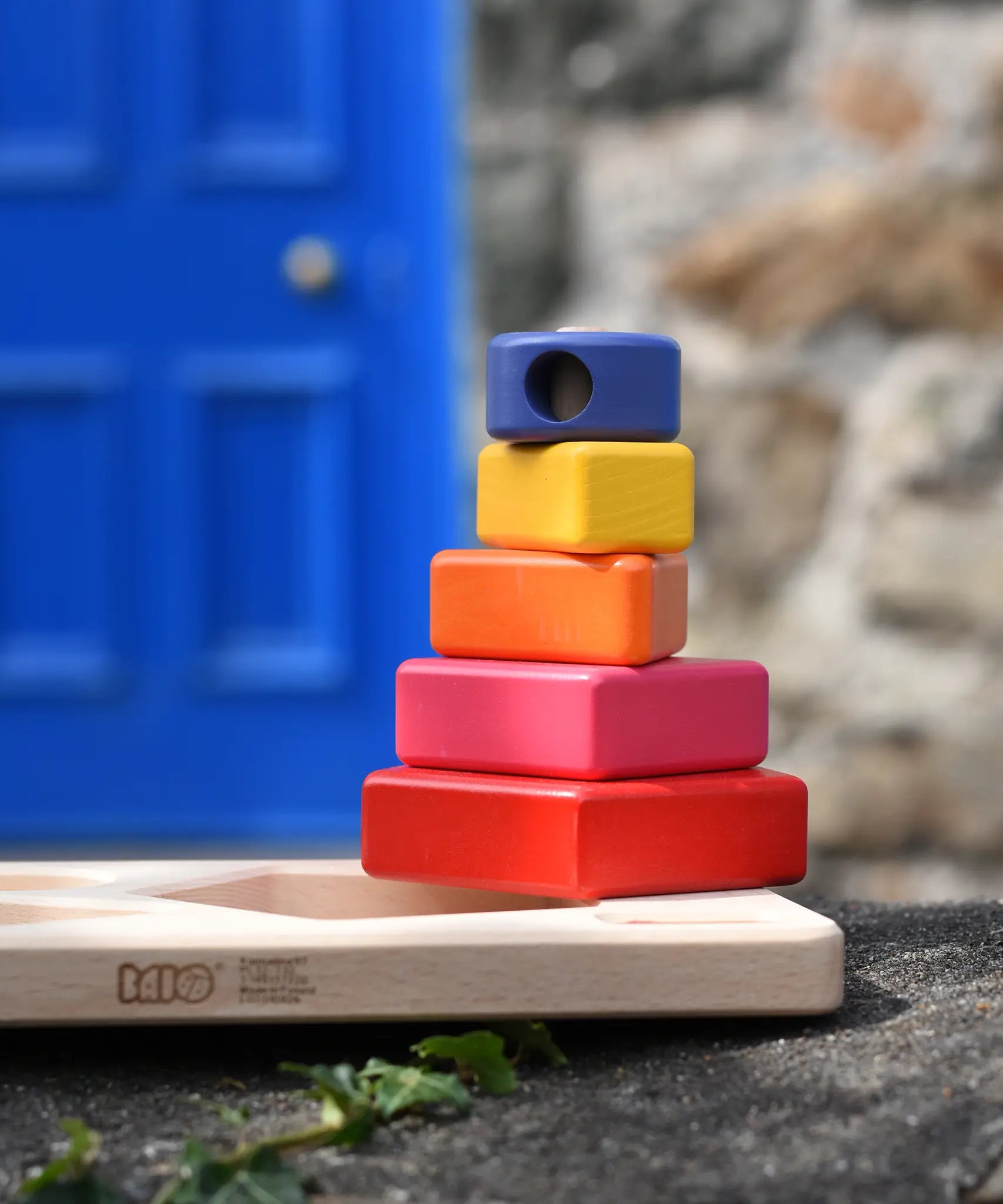 Bajo pyramid sorting board and stacker toy placed on a stone wall with the stacking pole with shapes on placed on the board base.