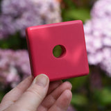 Pink square from the Bajo pyramid sorting board and stacker toy in an adult's hand.