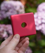 Pink square from the Bajo pyramid sorting board and stacker toy in an adult's hand.