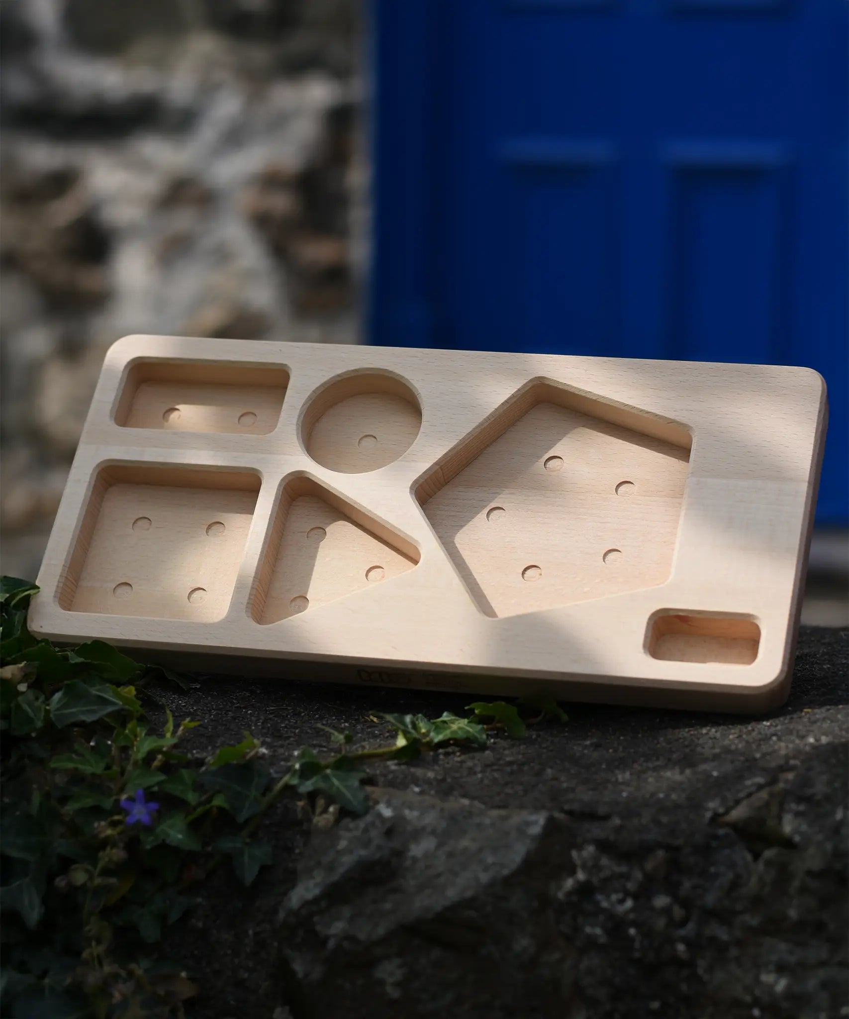 Board base from the Bajo pyramid sorting board and stacker toy placed on a stone wall.