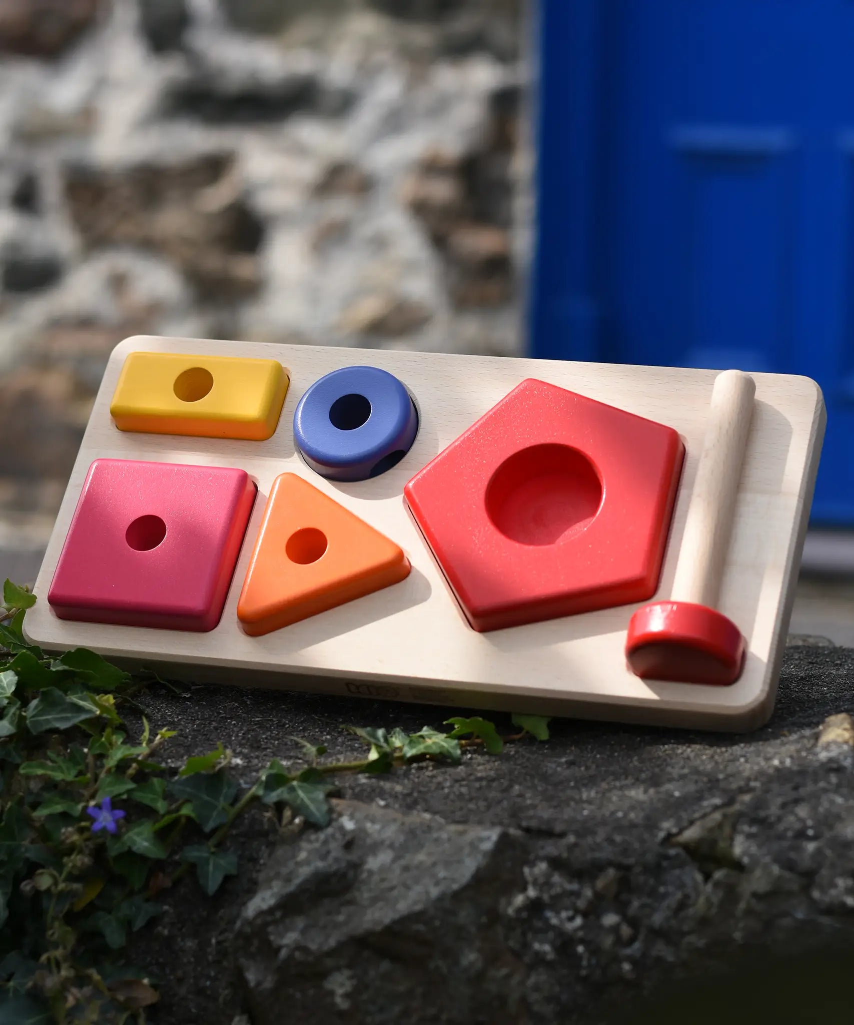 Bajo pyramid sorting board and stacker toy placed on a stone wall.