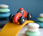 A red Bajo LR car placed on a yellow wooden arch. The car is a part of a wide range of Bajo wooden toy vehicles available at Babipur.
