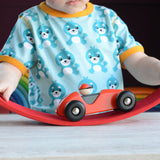 A close up of a child playing with a red Bajo LR car. The child is pushing the car over a red wooden arch. The car is a part of a wide range of Bajo wooden toy vehicles available at Babipur.