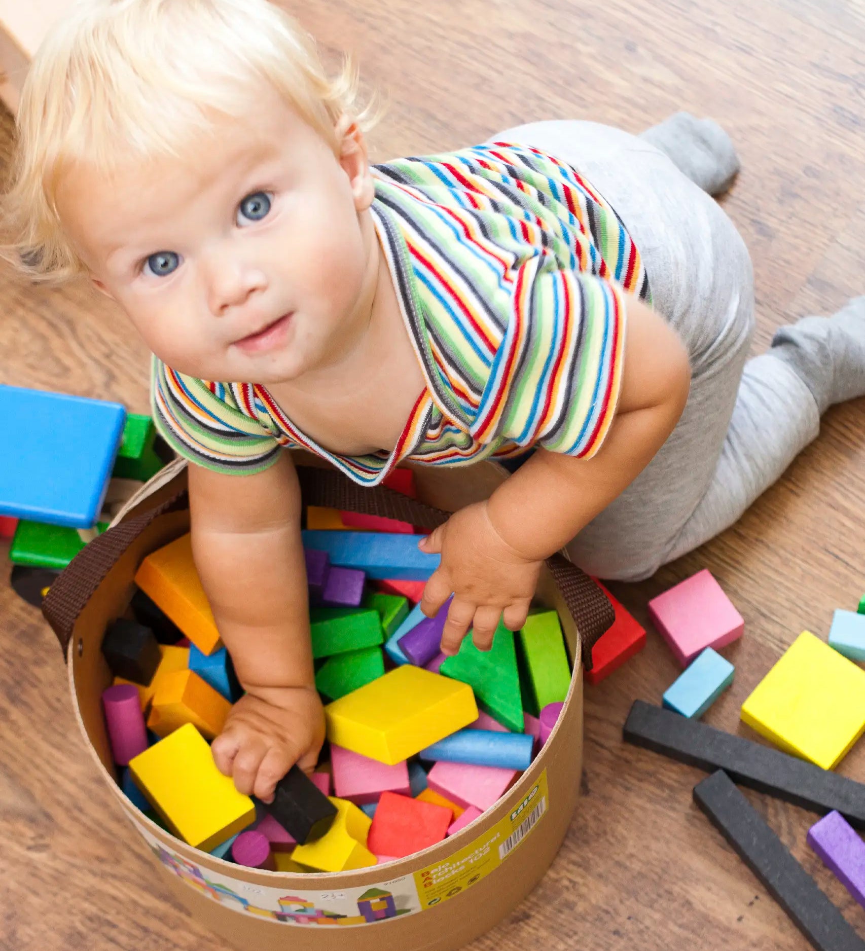 Toddler reaching into a full tub of Bajo wooden rainbow blocks 