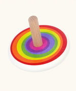 Bajo Rainbow Spinning Top. A white painted body with a rainbow design on the top and a natural wooden handle.