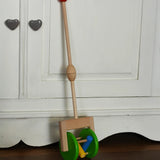 Bajo push along wooden toy rattle leaning against a white cupboard. Green rollers with coloured pieces in the middle 