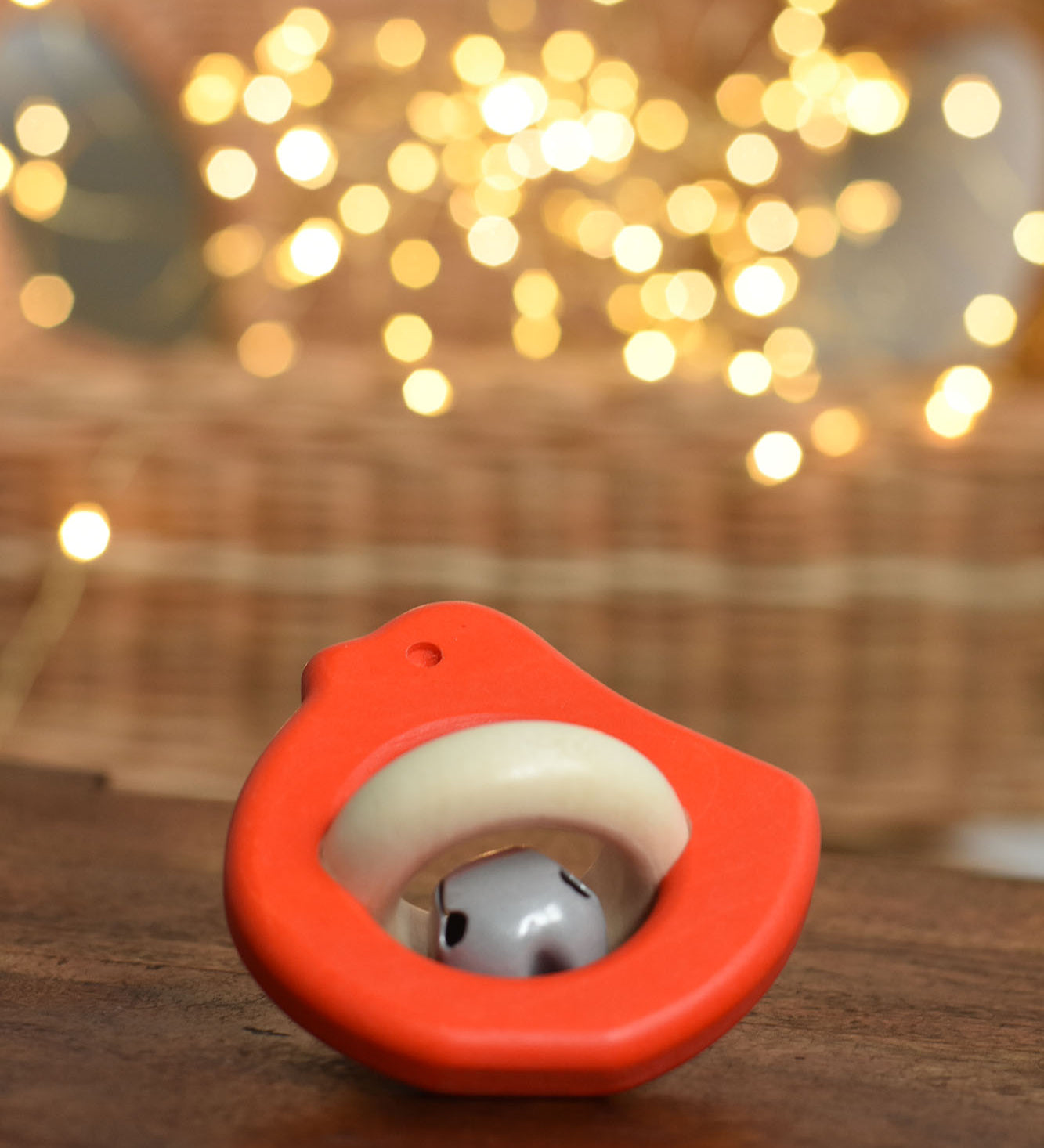 A red coloured Bajo Wooden Bird Baby Rattle with Bell placed on a small wooden table. These heirloom quality toys by Bajo are part of a wide range of wooden toys available here at Babipur. 