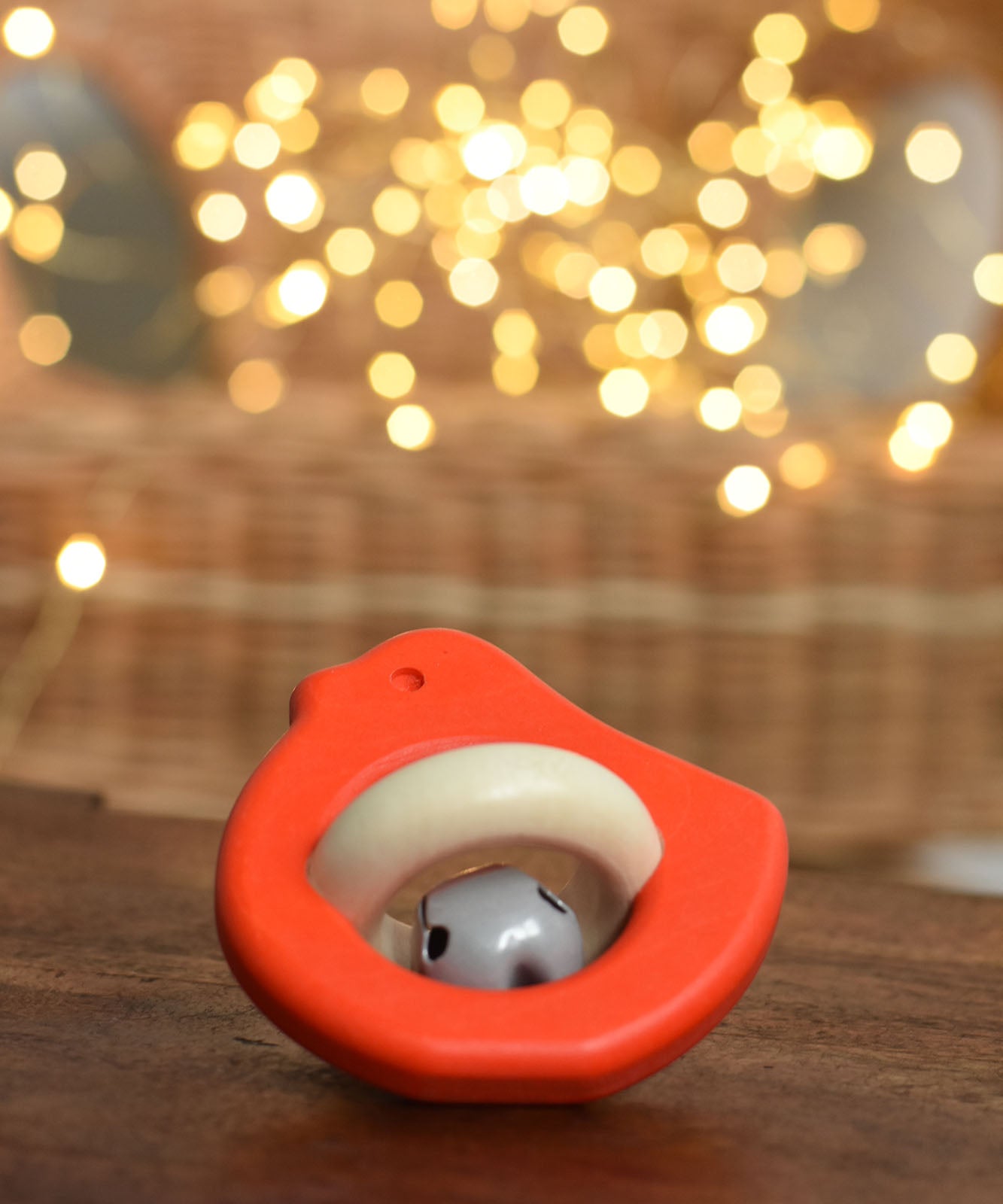 A red coloured Bajo Wooden Bird Baby Rattle with Bell placed on a small wooden table. These heirloom quality toys by Bajo are part of a wide range of wooden toys available here at Babipur. 