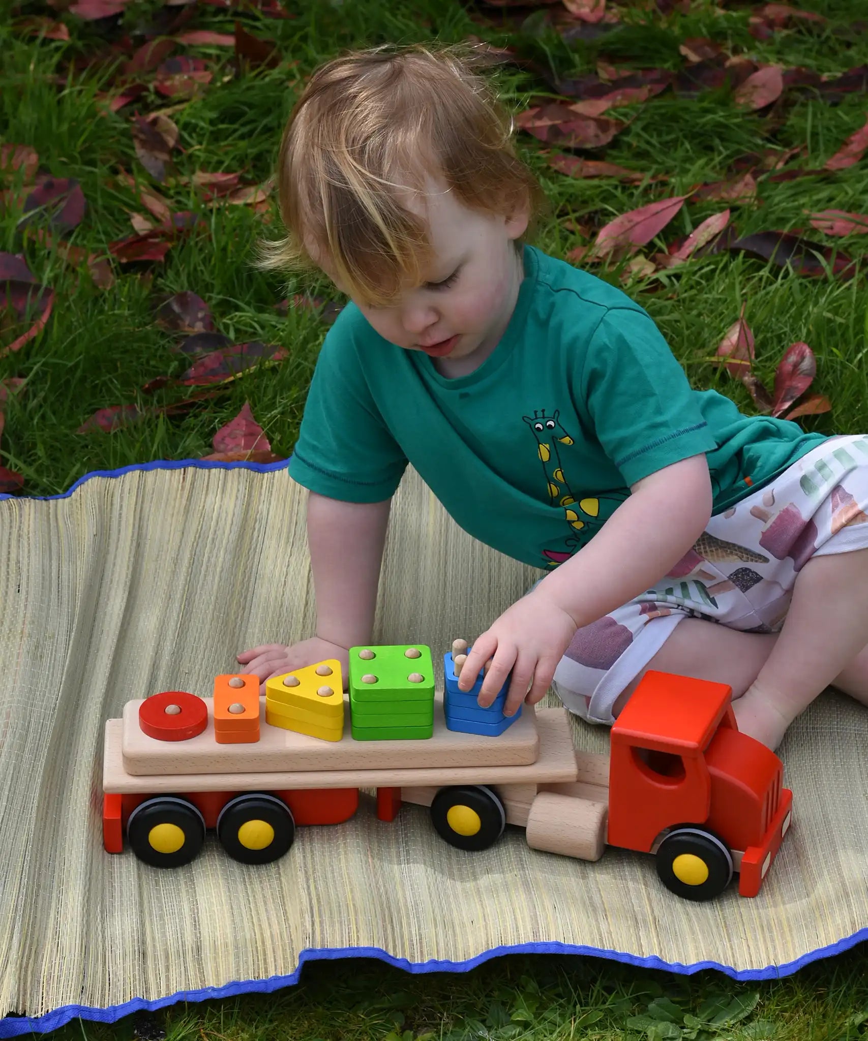 Child playing Bajo large red cargo truck and wooden shape sorter toy outdoors. 