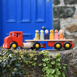 Bajo large red cargo truck and wooden shape sorter toy placed on a stone wall with Grapat wild crew wooden peg dolls placed on the back.