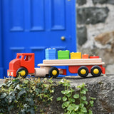 Bajo large red cargo truck and wooden shape sorter toy placed on a stone wall outdoors.