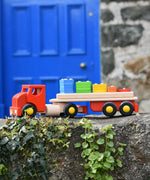 Bajo large red cargo truck and wooden shape sorter toy placed on a stone wall outdoors.