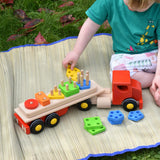Child playing with the Bajo large red cargo truck and wooden shape sorter toy outdoors.