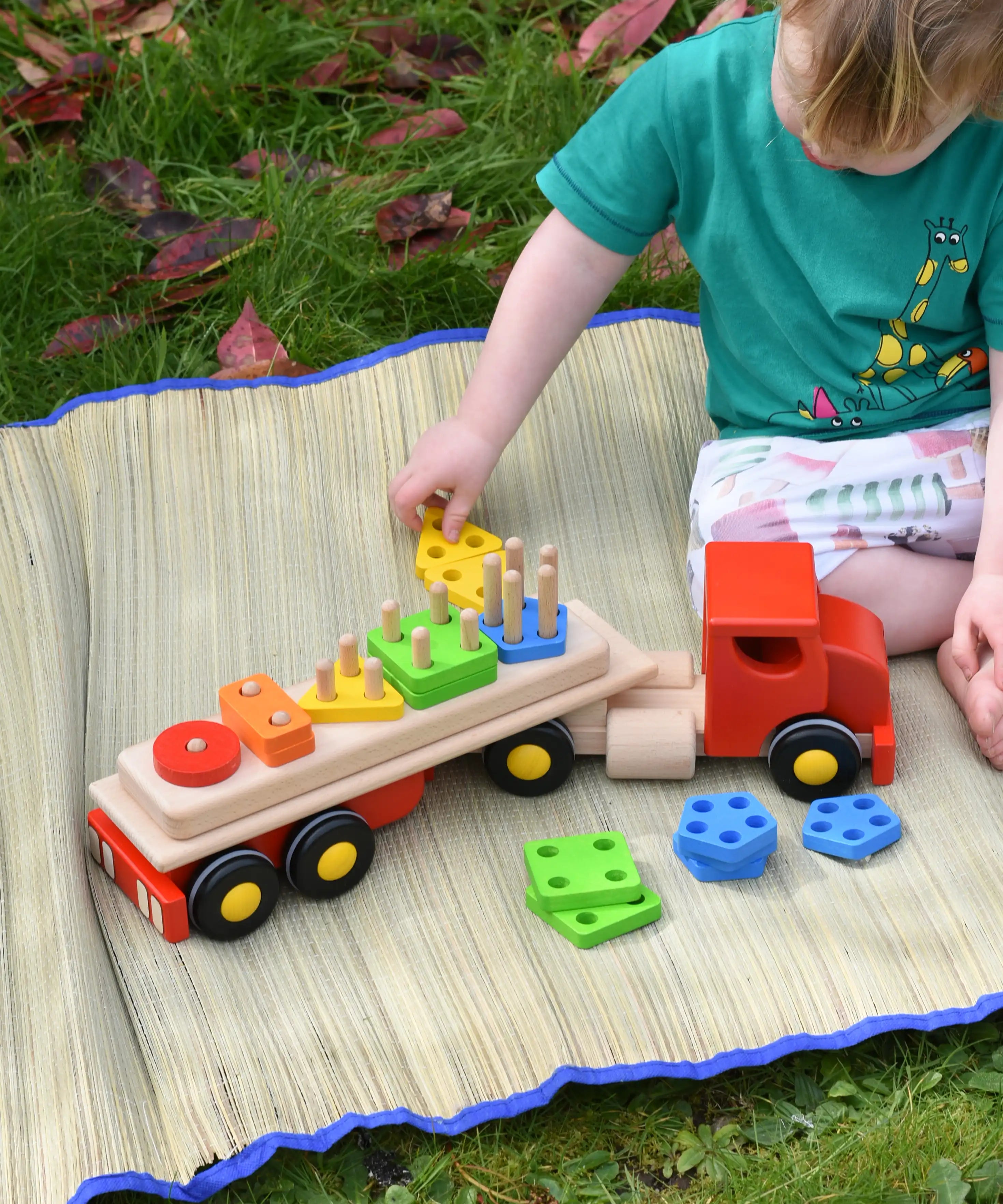Child playing with the Bajo large red cargo truck and wooden shape sorter toy outdoors.