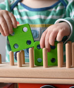 Close up of child placing green square shapes on the back of the Bajo large red cargo truck and wooden shape sorter toy.