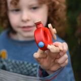 A child holding up a Bajo Red Fire Engine Helicopter wooden toy. The red coloured wooden helicopter has natural propellers and stand and a blue lamp details on the front. These heirloom quality toys by Bajo are part of a wide range of wooden toys available here at Babipur. 