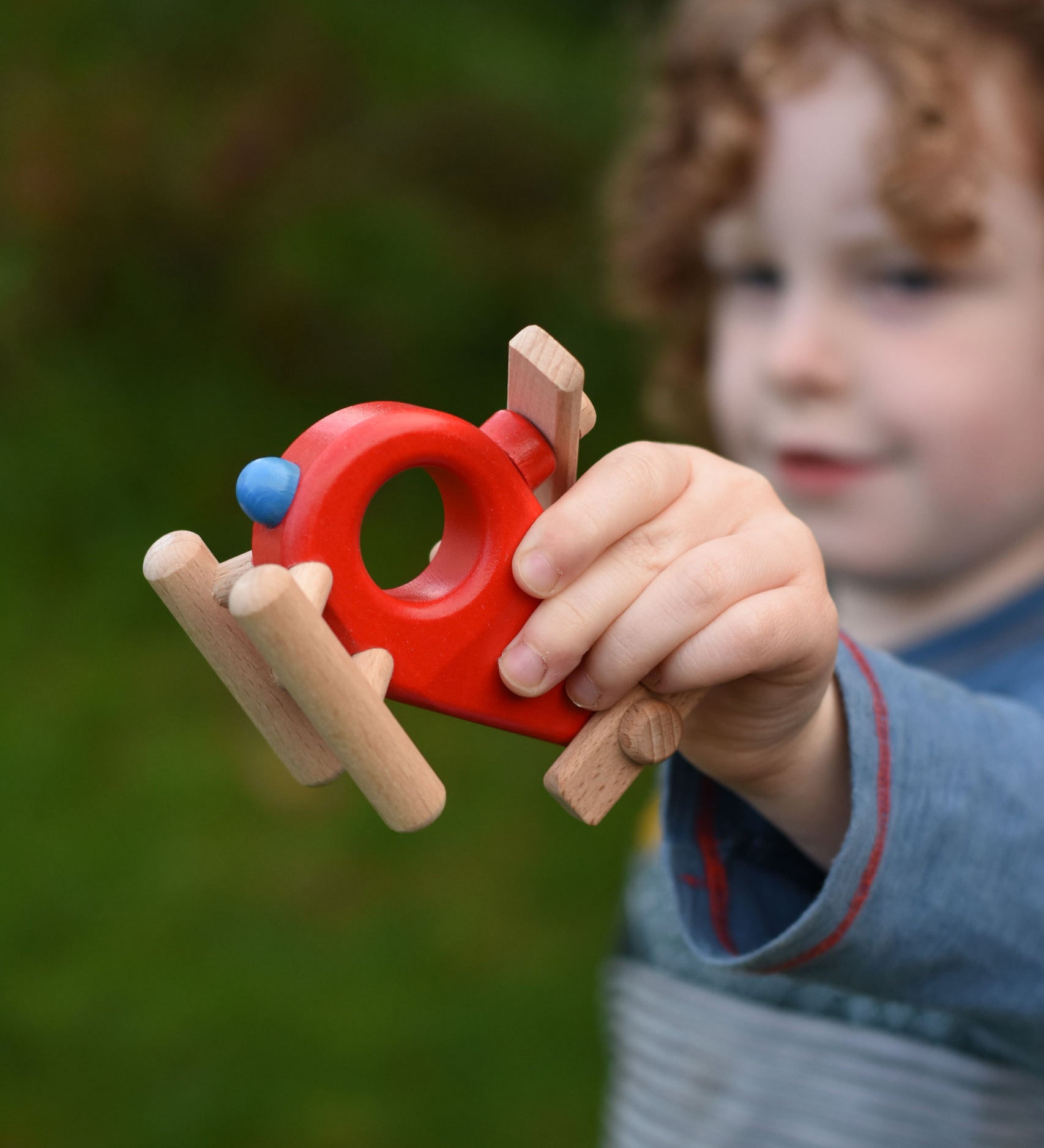 A child playing with the Bajo Red Fire Engine Helicopter wooden toy. The red coloured wooden helicopter has natural propellers and stand and a blue lamp details on the front. These heirloom quality toys by Bajo are part of a wide range of wooden toys available here at Babipur. 
