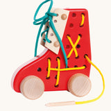 Bajo red Lacing Shoe wooden toy. A red boot shaped threading toy with wheels. These heirloom quality toys by Bajo are part of a wide range of wooden toys available here at Babipur. 