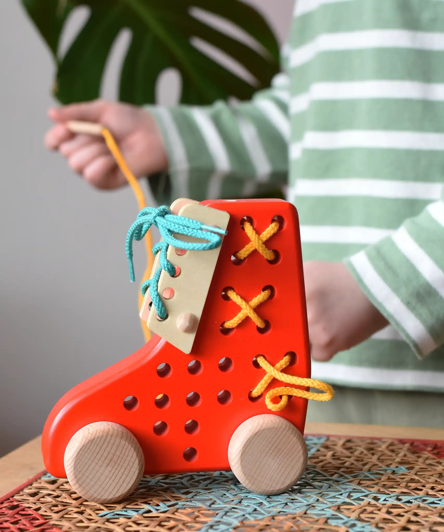 Bajo red lacing shoe wooden push along toy placed on a rattan stool in the Babipur playroom.
