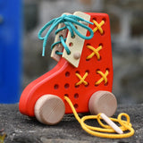 Bajo red lacing shoe wooden push along toy placed on a stone wall.