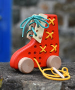 Bajo red lacing shoe wooden push along toy placed on a stone wall.