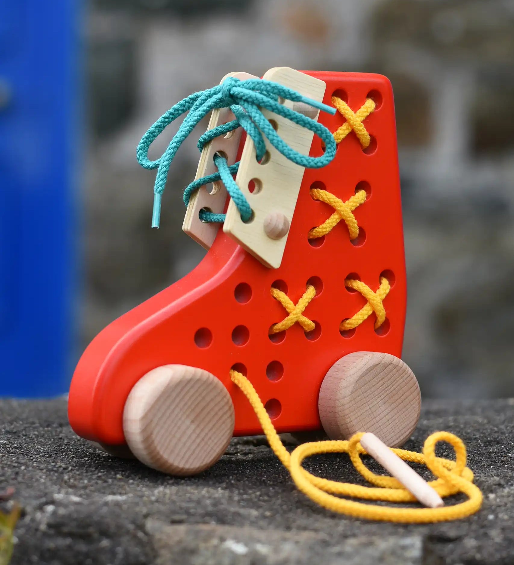 Bajo red lacing shoe wooden push along toy placed on a stone wall.