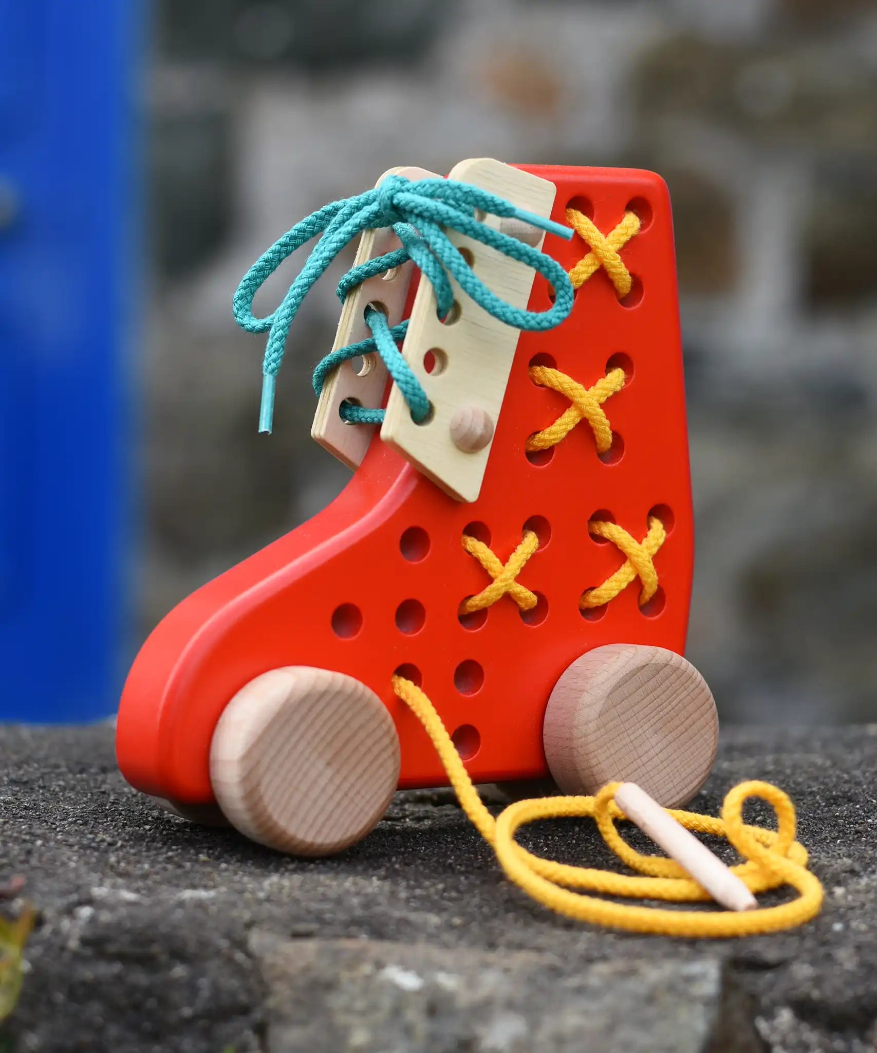 Bajo red lacing shoe wooden push along toy placed on a stone wall.