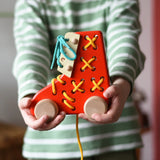 Bajo red lacing shoe wooden push along toy in a child's hands