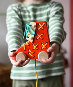 Bajo red lacing shoe wooden push along toy in a child's hands
