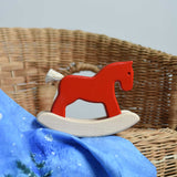 A red coloured Bajo Mini Rocking Horse placed on a child's wicker chair.  These heirloom quality toys by Bajo are part of a wide range of wooden toys available here at Babipur. 