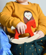 A child holding a red coloured Bajo Mini Rocking Horse on their lap. These heirloom quality toys by Bajo are part of a wide range of wooden toys available here at Babipur. 