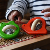 Bajo red snail rattle and green frog baby toys placed on a rattan stool.