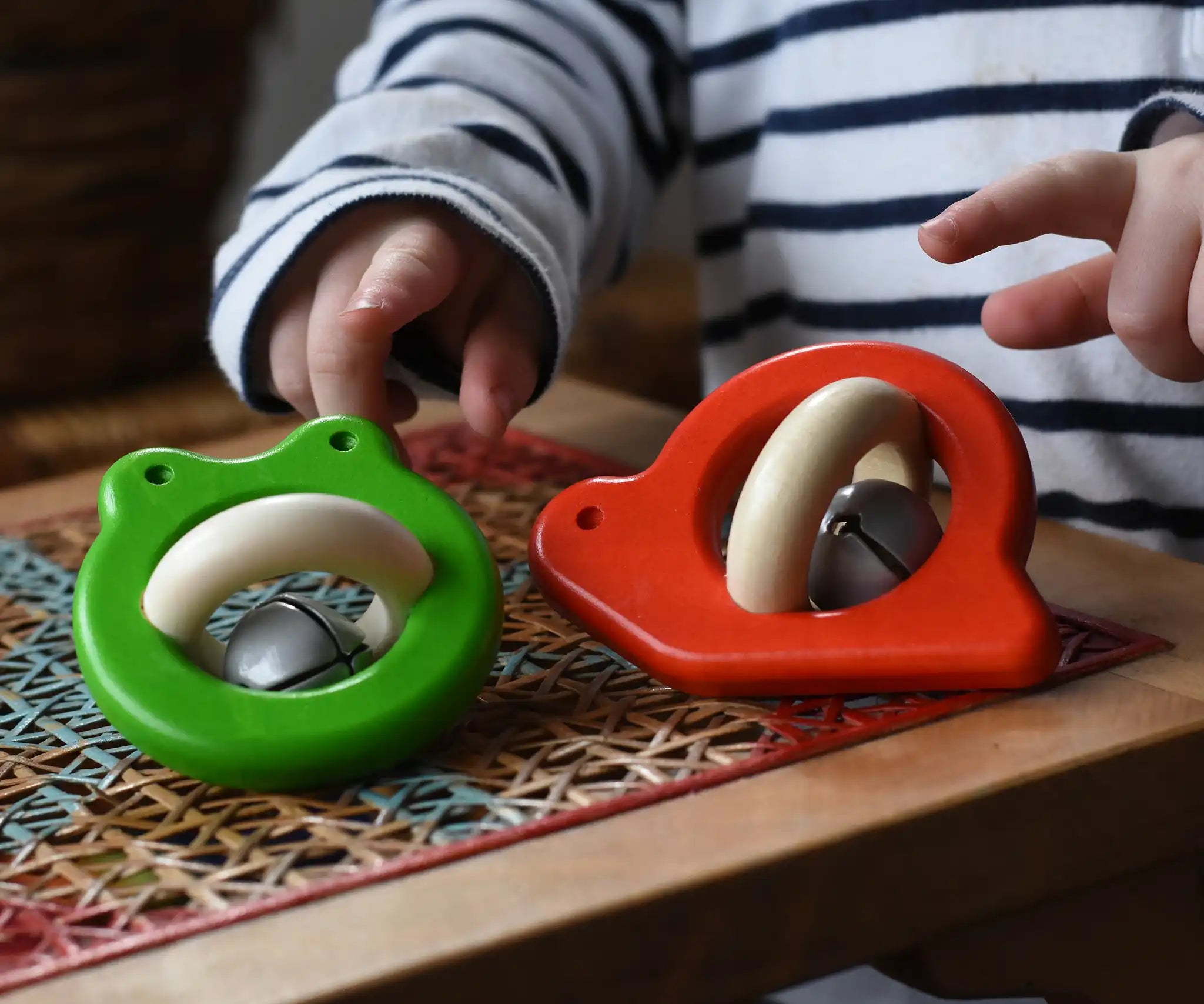 Bajo red snail rattle and green frog baby toys placed on a rattan stool.