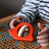 Choild reaching for the Bajo red snail rattle baby toy placed on a rattan stool.
