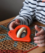 Choild reaching for the Bajo red snail rattle baby toy placed on a rattan stool.