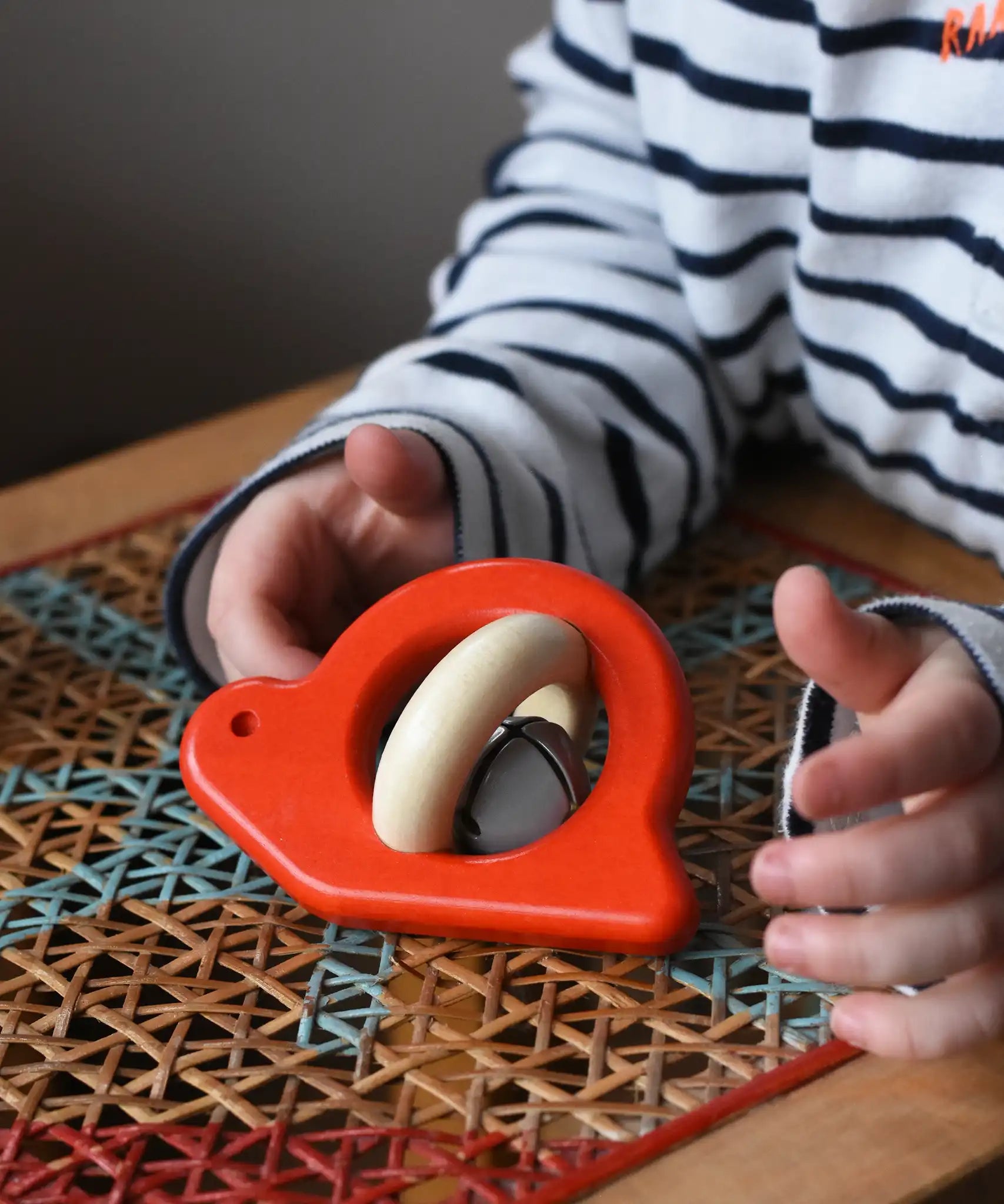 Choild reaching for the Bajo red snail rattle baby toy placed on a rattan stool.
