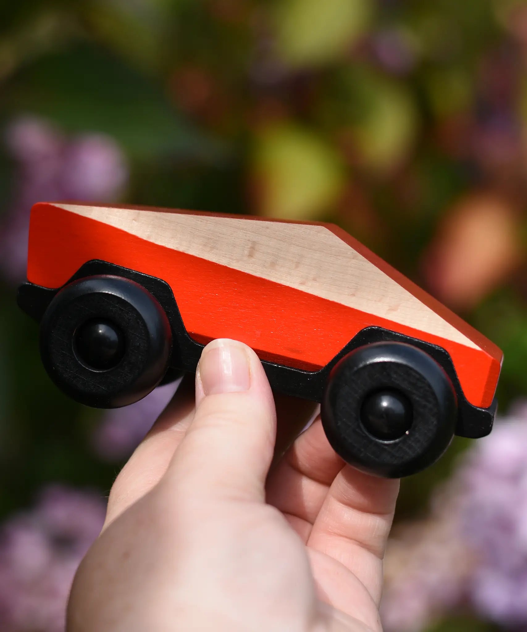 Bajo red ToBe Poly car wooden toy in an adult's hand.