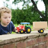 A child playing with the Bajo tractor and trailer outdoors. The tractor has a  red, green and blue painted finish and natural wood trailer. These heirloom quality toys by Bajo are part of a wide range of wooden toys available here at Babipur.