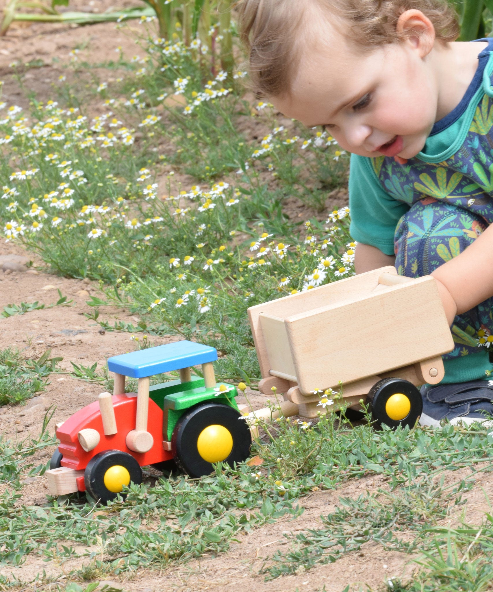A child playing with the Bajo tractor and trailer outdoors. These heirloom quality toys by Bajo are part of a wide range of wooden toys available here at Babipur.