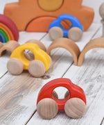 A group of Bajo handmade wooden beetle style car including blue, yellow and red available at Babipur. Cars have unpainted wheels and can be pulled or pushed along.